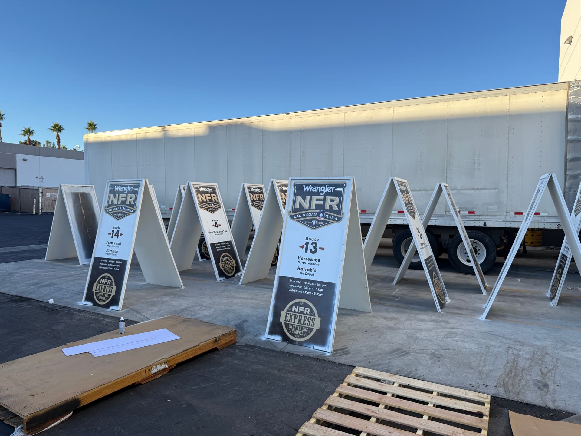 Rows of A-frame wayfinding signs lined up outdoors beside a trailer