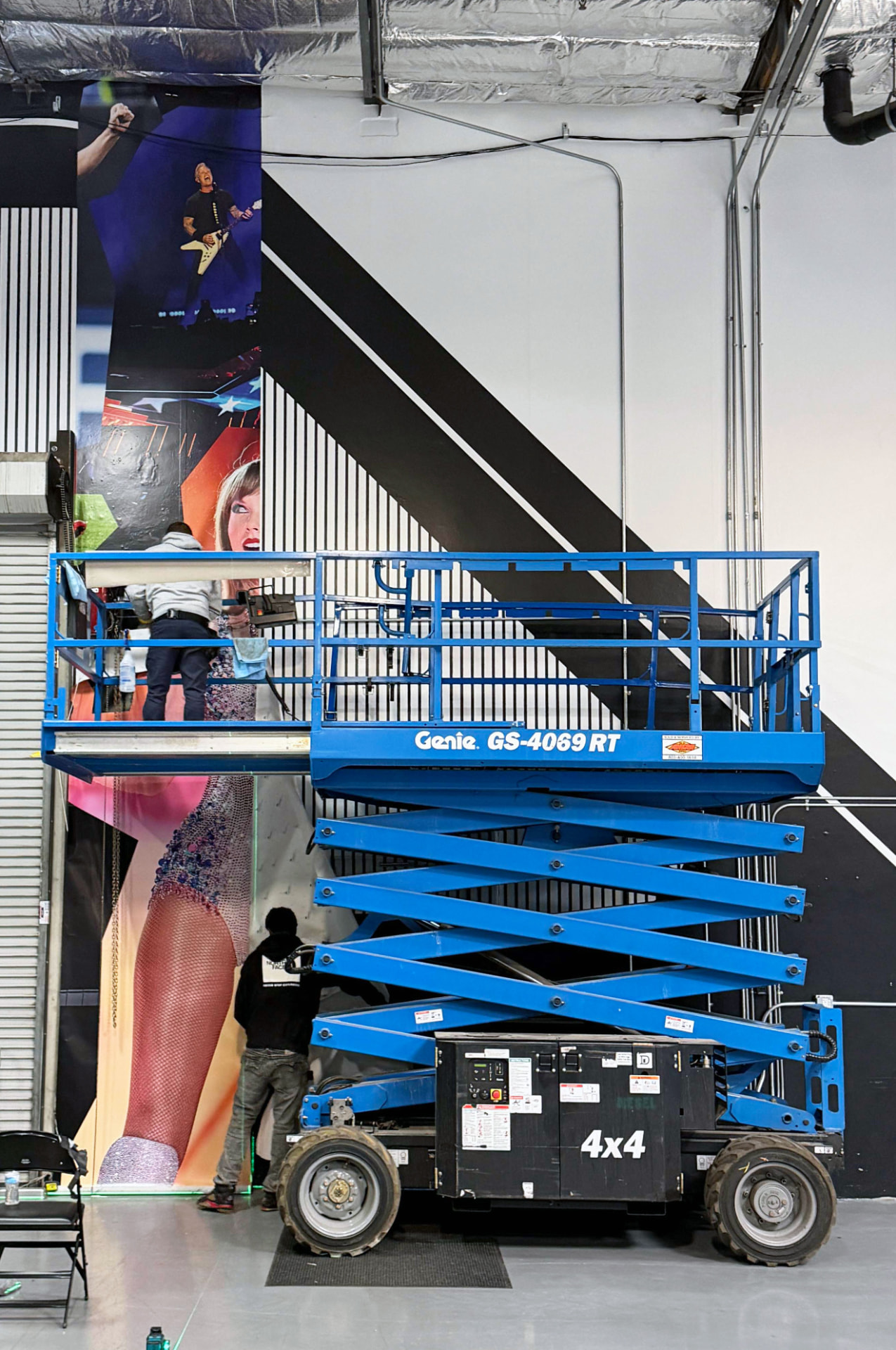 Two installers applying a tall printed wall graphic from a scissor lift