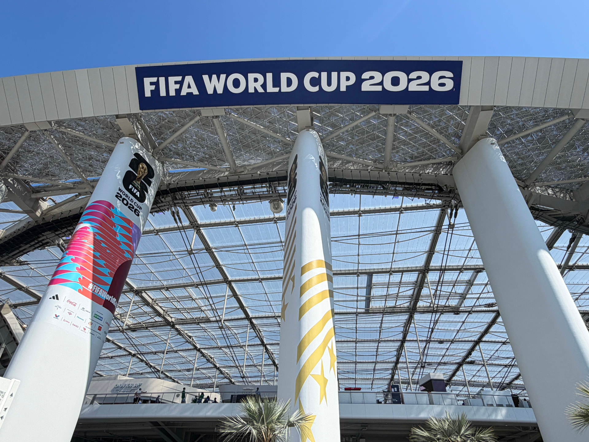 Stadium entrance with oversized wrapped columns and a large overhead banner, visitors walking below