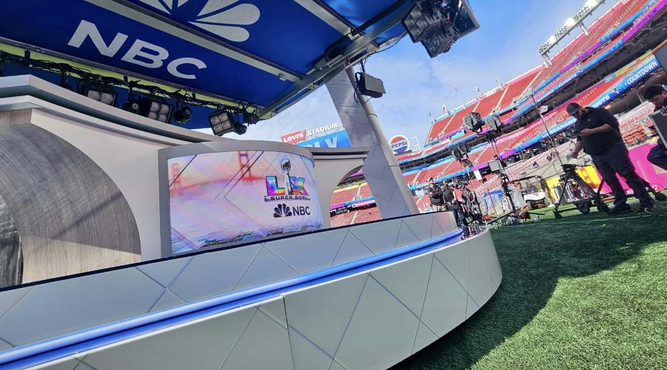 Angled view of the NBC broadcast set with Super Bowl LX screen, lighting rig and crew in the stadium