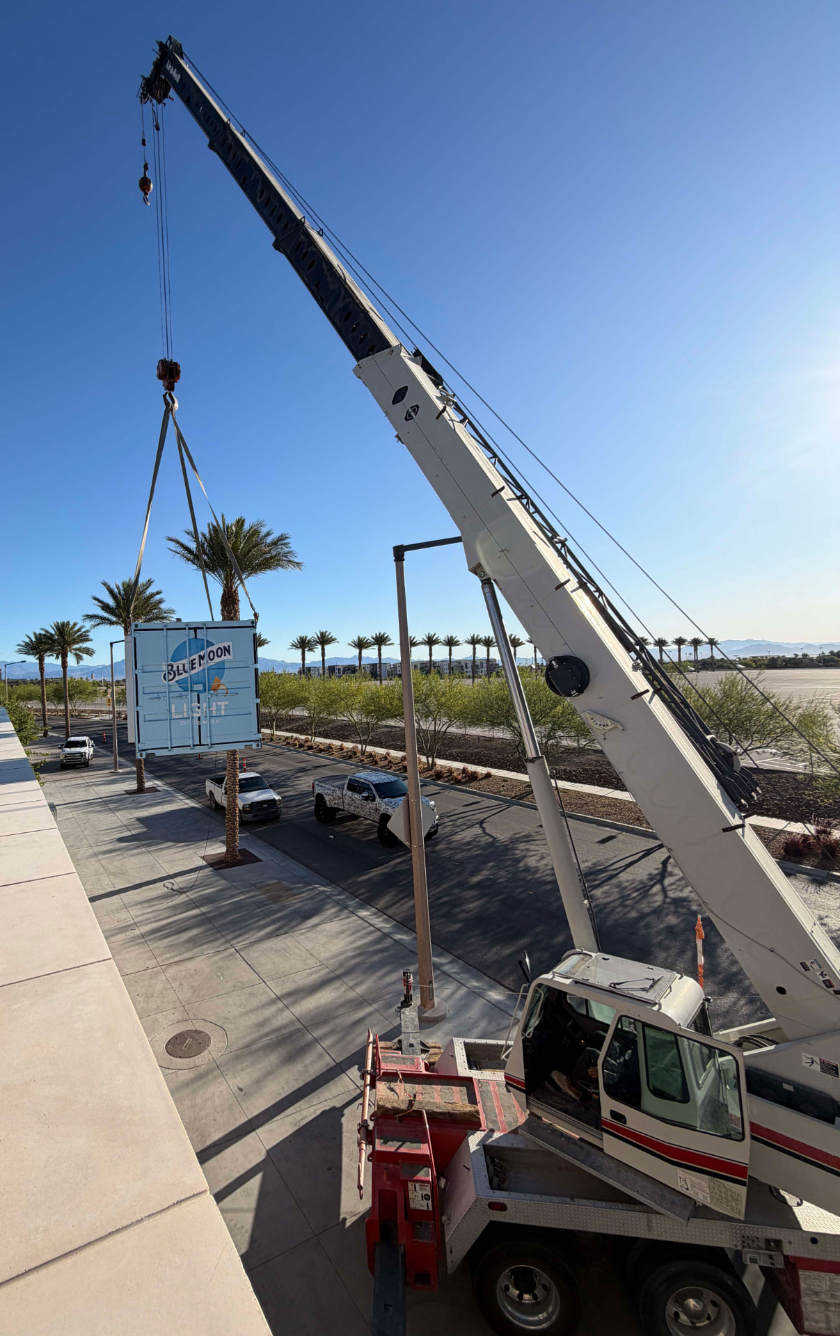 Mobile crane lifting a large printed shipping-container sign into place
