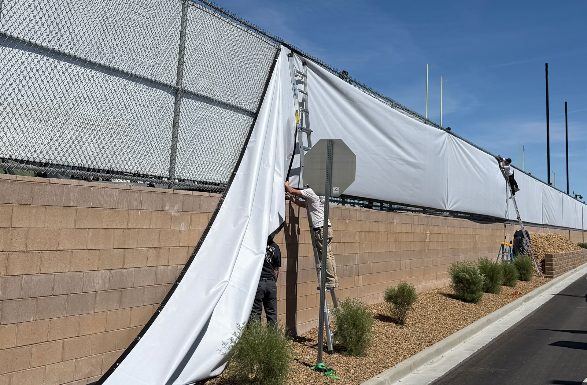 Installers on ladders hanging a long fence banner along a block wall