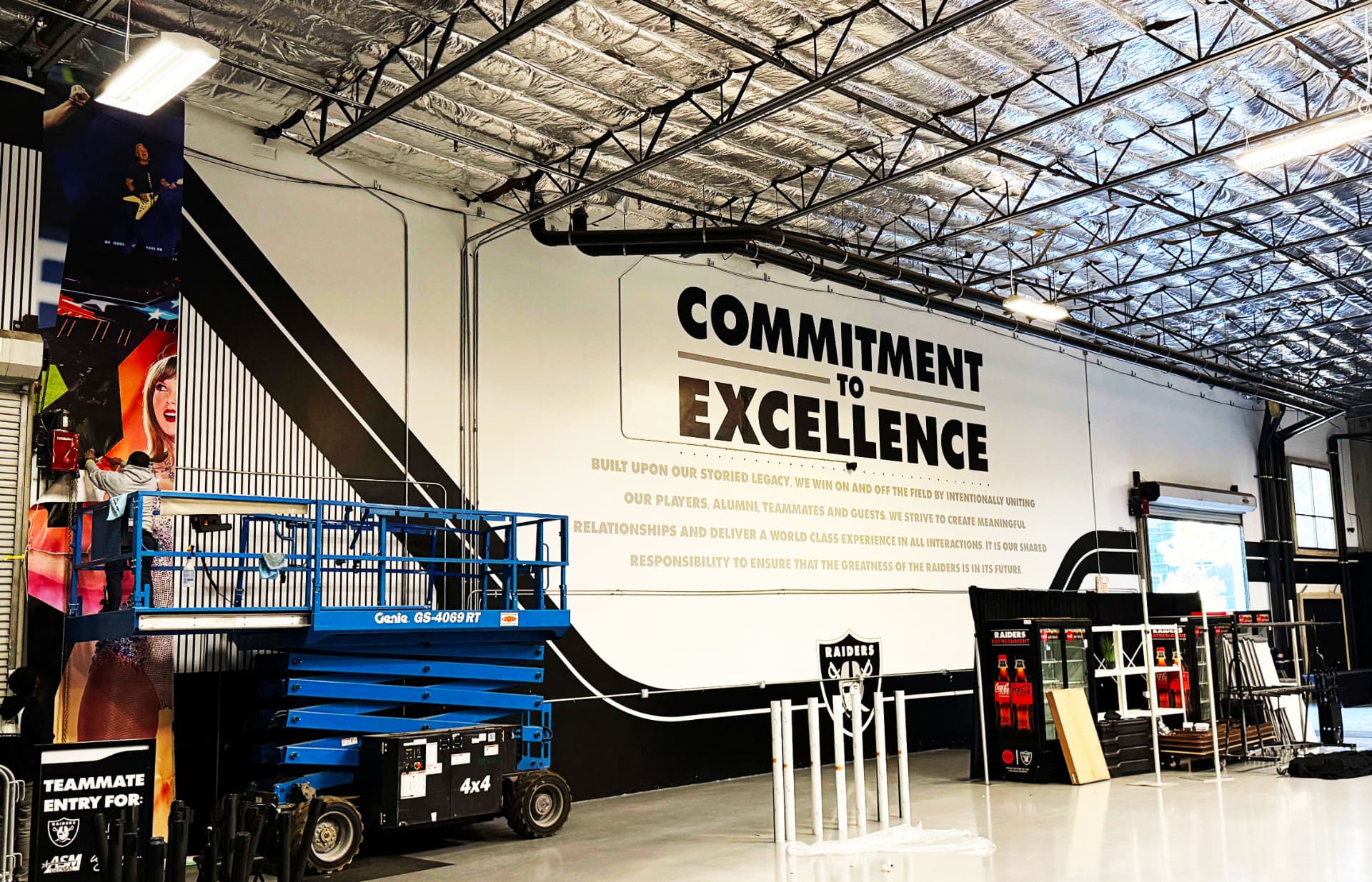 Installers on a scissor lift applying wall graphics inside a large warehouse space